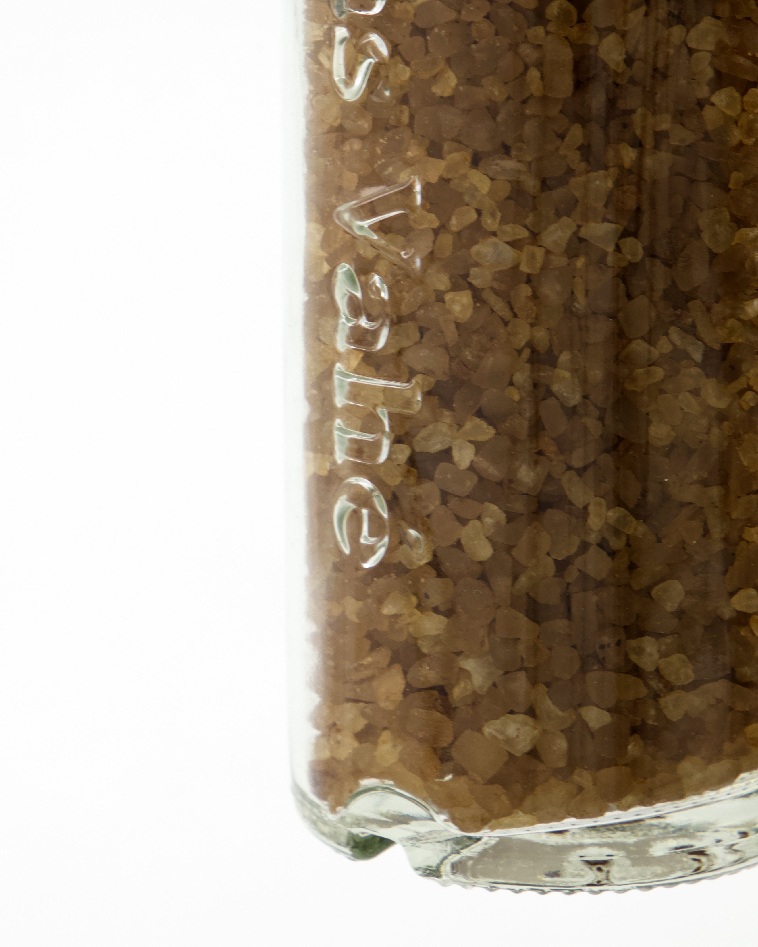 A close-up of a clear glass jar of Nicolas Vahé Salt, Smoked, filled with coarse brown beechwood-smoked sea salt granules. Part of the jar's embossed text is visible against a plain white background.
