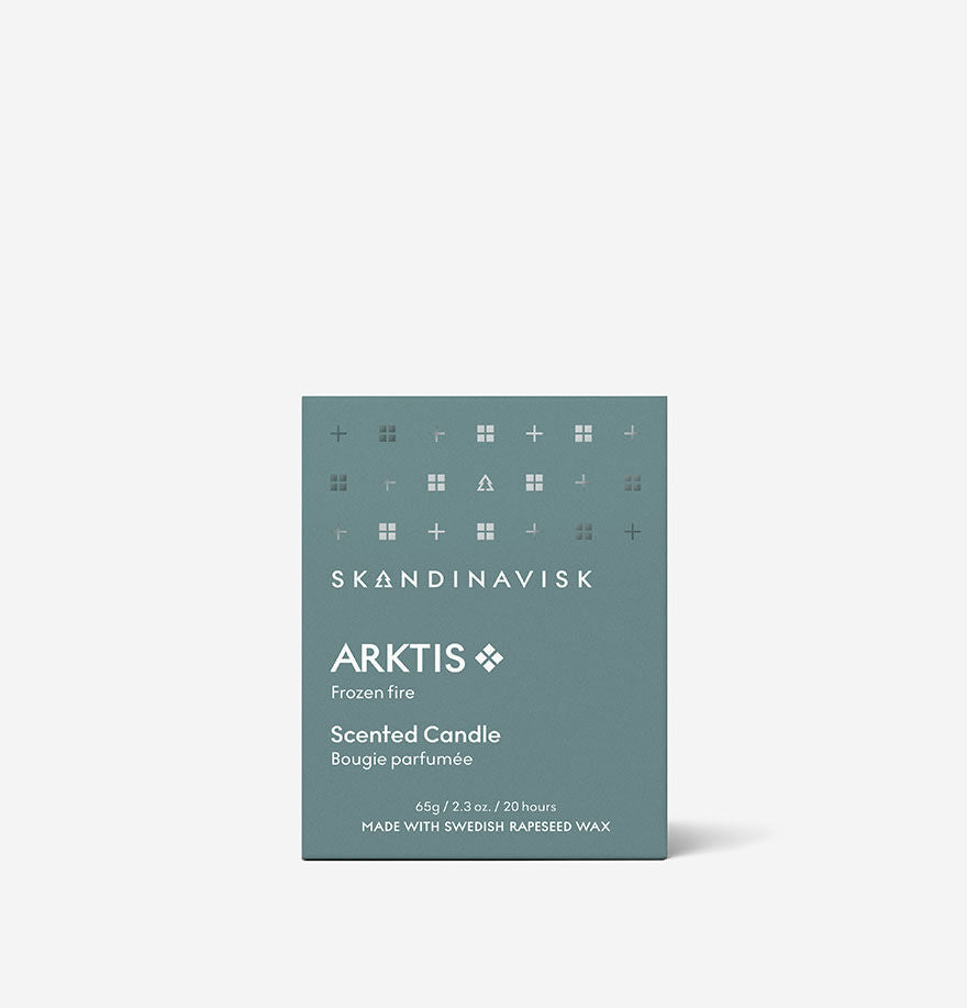 A box labeled Skandinavisk Mini Scented Candle Arktis, 65 g in teal features small minimalist icons and text indicating it is made with Swedish rapeseed wax. The elegantly painted glass candle brings a modern flair to any space while capturing the essence of the far north.