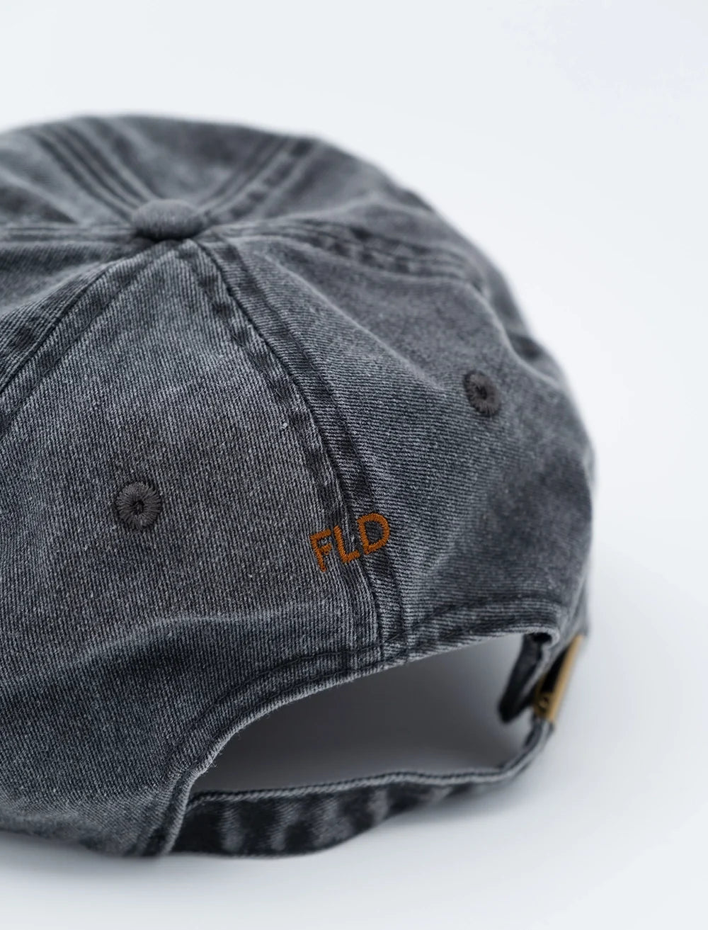 A close-up of the back of the Fine Little Day Giro Bike Cap Embroidered in Vintage Black, a faded black denim 6-panel strapback hat featuring brown FLD embroidery and an adjustable strap, reminiscent of a classic embroidered biker’s hat.