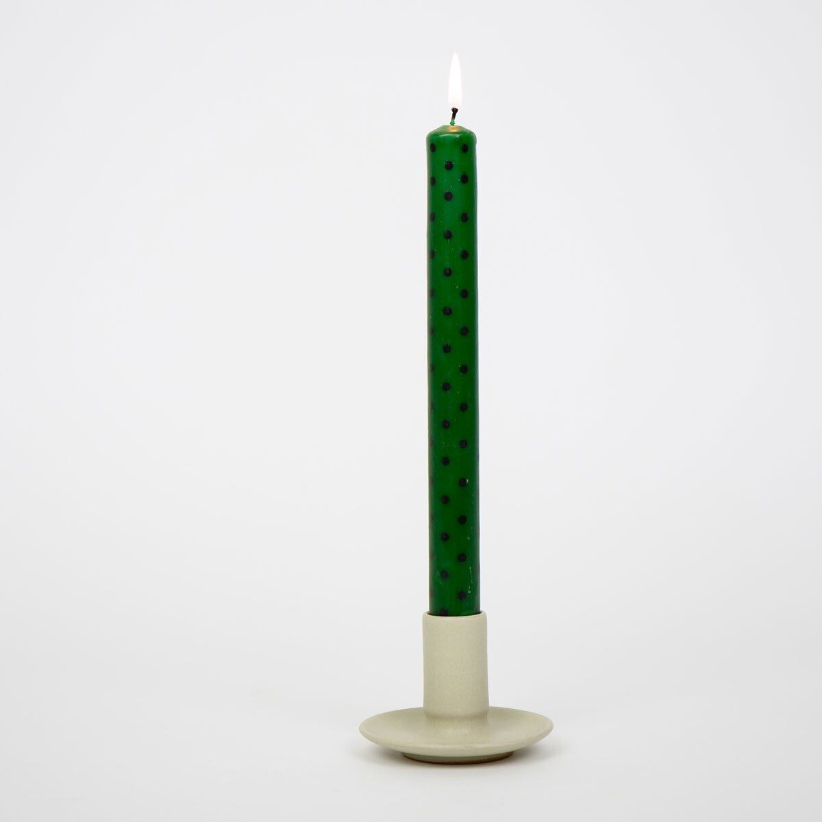 A lit Candles Minidot Green & Black, Handmade 2 Pack taper candle with black polka dots held in a simple, neutral-toned candle holder.