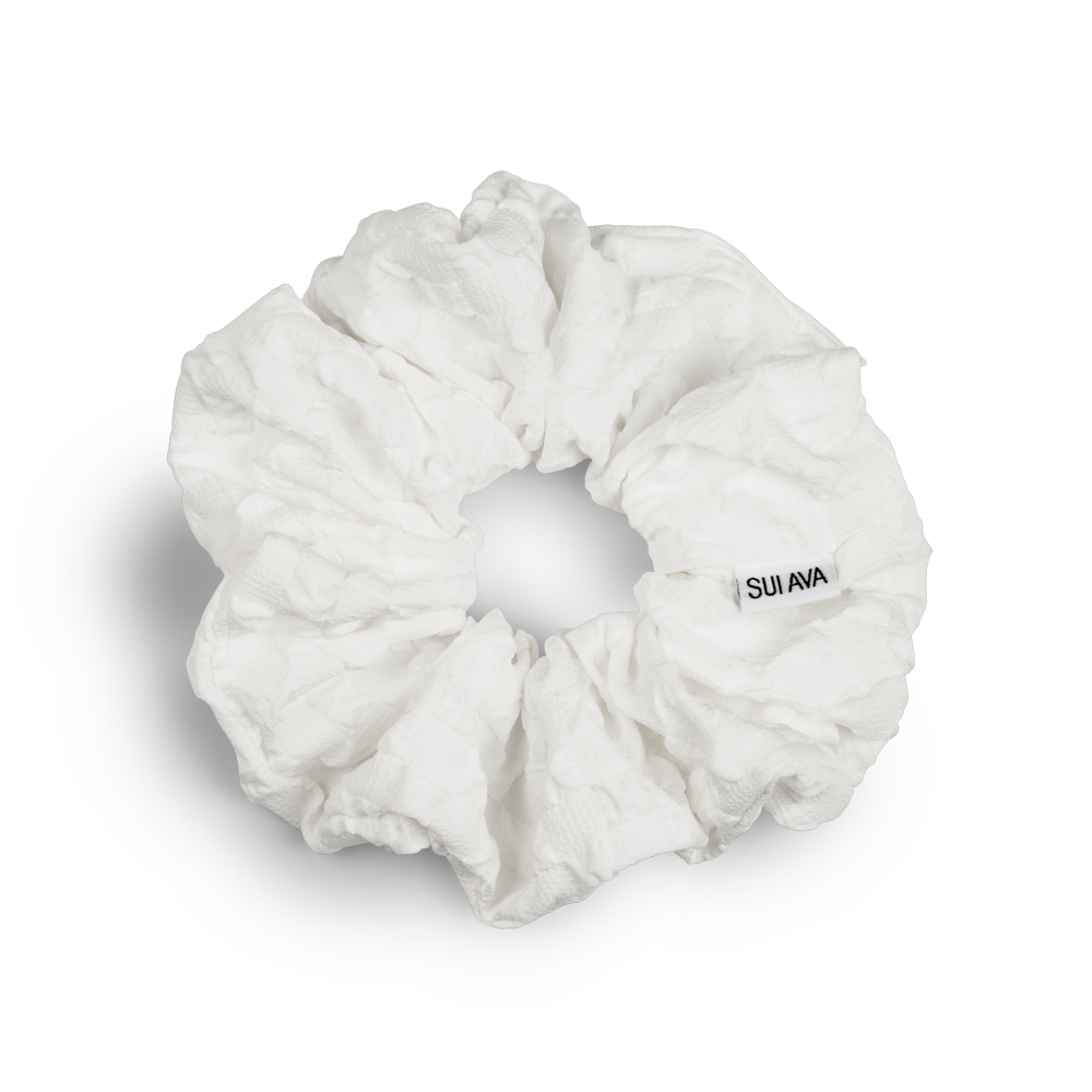 The Daydream Scrunchie in White by Sui Ava features textured white fabric and a subtle Sui Ava tag, shown against a plain white background. This stylish accessory adds an elegant touch to any look.