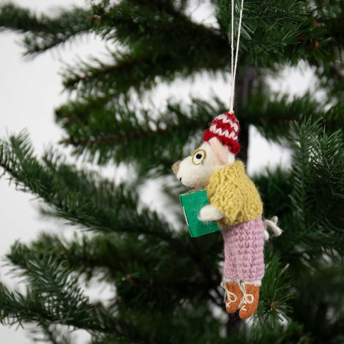 A Reading Teacher Christmas Ornament, Handmade in Wool, featuring a felted mouse in a knit sweater and hat holding a book, hanging from a Christmas tree branch with literary charm.