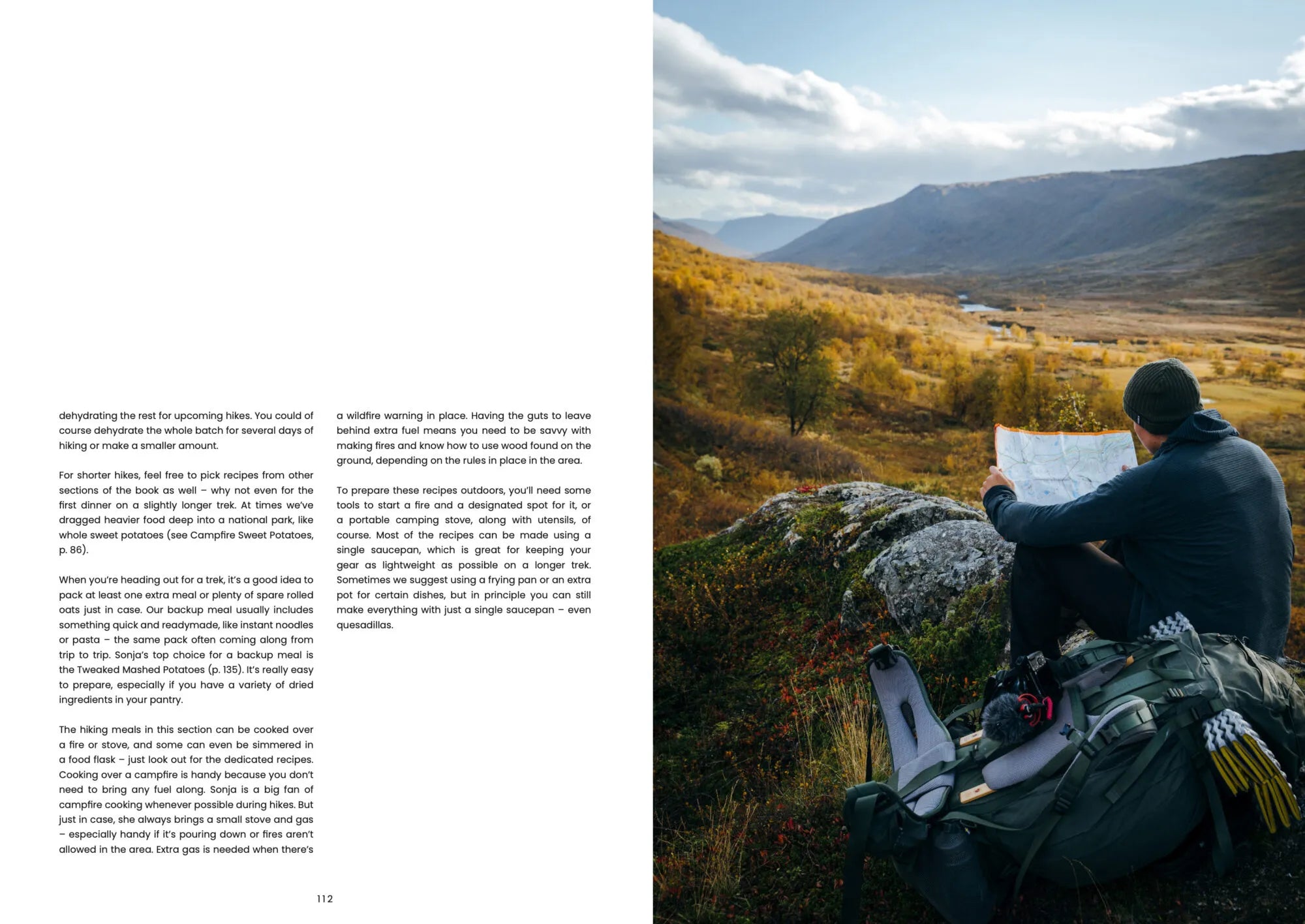 A hiker with a backpack sits on a rock, studying a map while gazing over a breathtaking autumn valley filled with mountains, a winding river, and golden trees beneath partly cloudy skies. Nearby, camping gear is arranged alongside “Food Over the Campfire – Recipes for Day Hikes and Wilderness Treks” from Cozy Publishing, ready to inspire delicious vegetarian meals cooked right at the campsite.