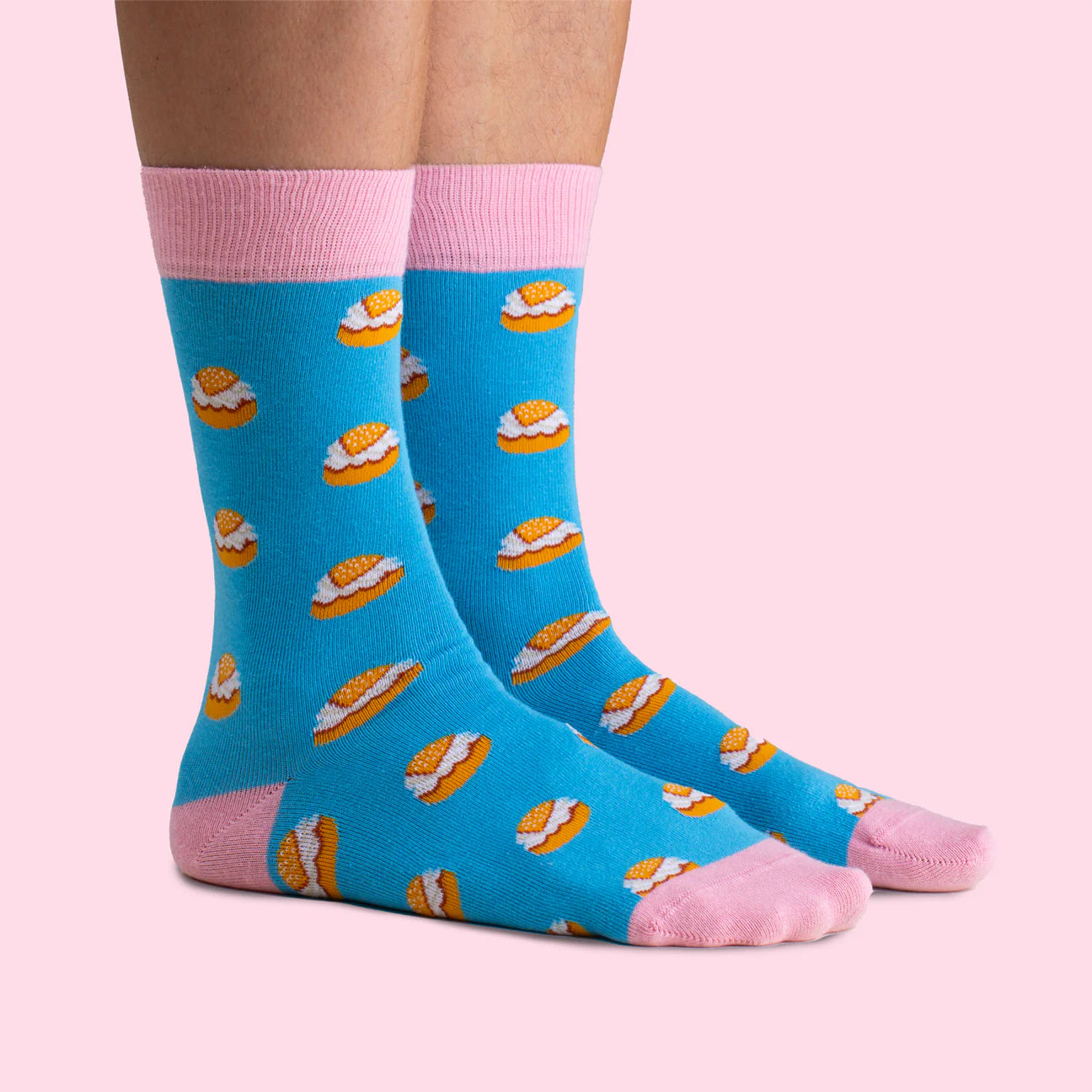 A person wears Svensk Husman Socks from the Fika Coffee Table Gift Box, featuring cozy blue socks with pink details and a playful coffee mug and cinnamon bun pattern—perfect as a gift for coffee lovers.