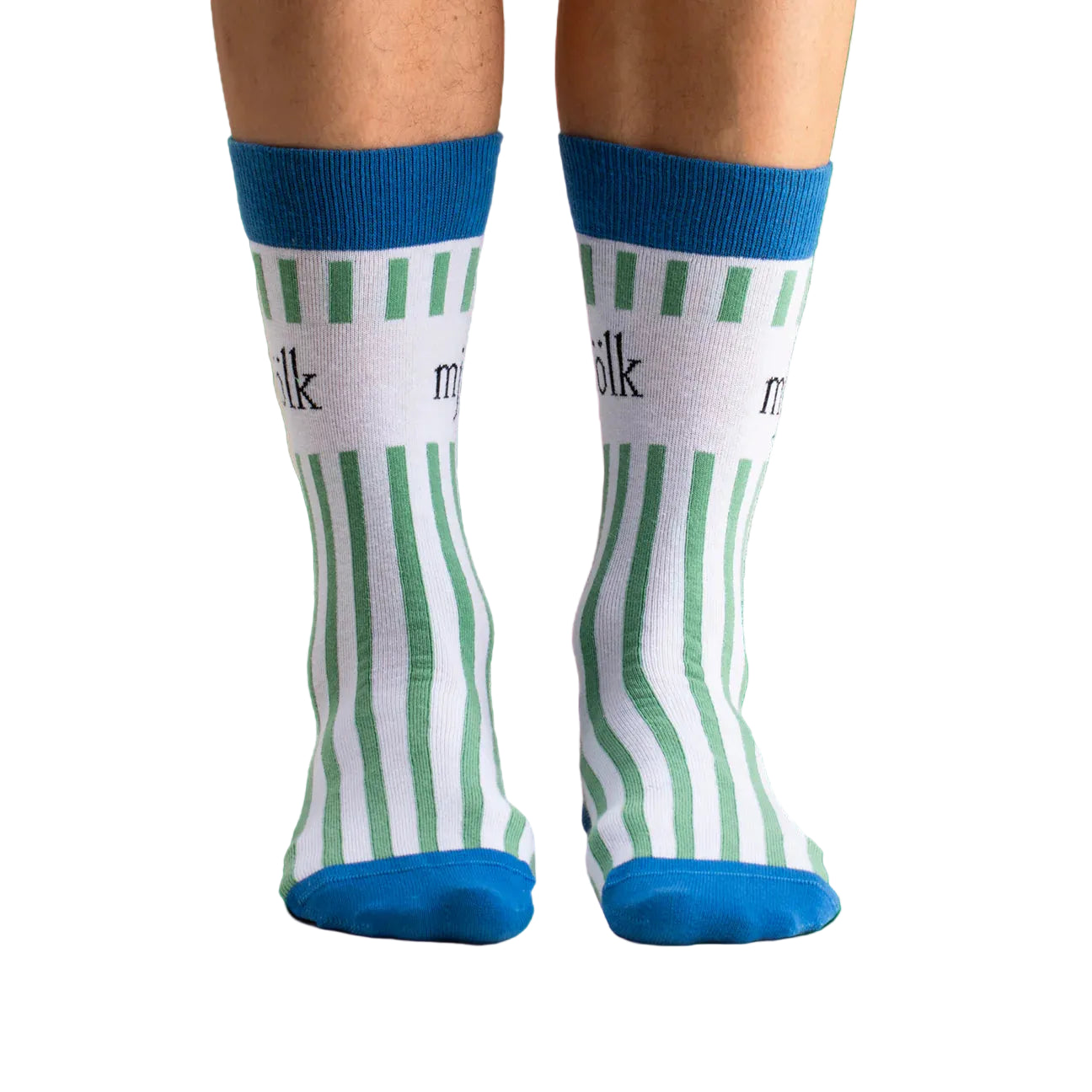 A pair of feet in Svensk Husman Socks' Grön Mjölk (Green Milk) socks—a cotton blend with white fabric, green vertical stripes, blue toes and cuffs, and "milk" printed in black near the top.