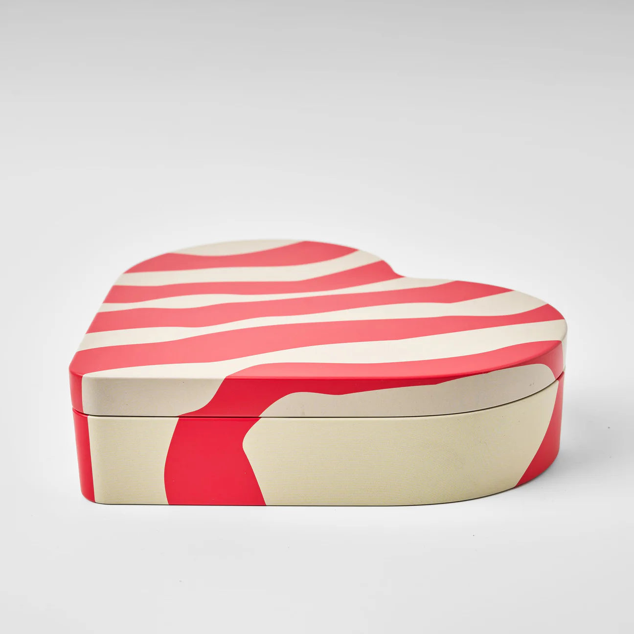 The Gåva Gifting Heart Reusable Tin - Älskar (Love) features a cream and red wavy striped pattern on its lid and sides, ideal for storing Swedish candy, displayed against a plain light gray background.