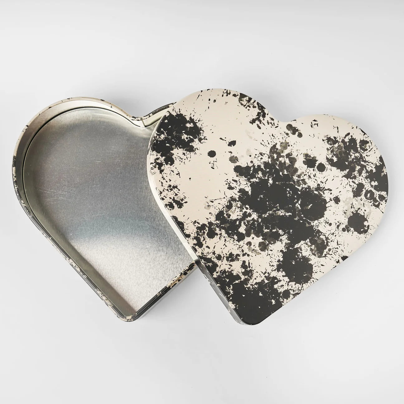 Gåva Gifting’s Heart Reusable Tin - Tack (Thank You) features a heart-shaped design with a partially removed lid, adorned with modern Swedish-inspired black splatters. The interior is plain silver—ideal as a reusable gift box against a white background.