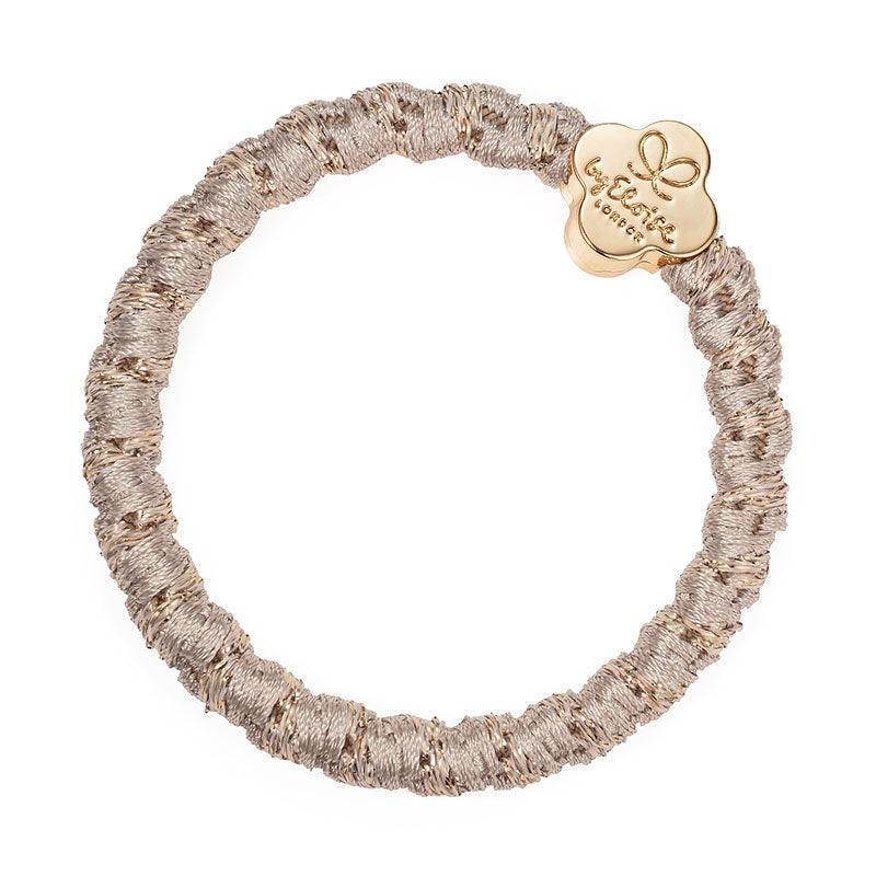 The ByEloise Bangle Band, Woven in Blonde with a Gold Quatrefoil charm, offers a stylish update to the classic hair band with its textured design and elegant gold detail.