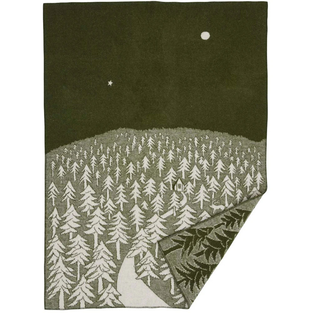 The House in the Forest Lambswool Blanket in Green by Klippan Yllefabrik features a charming forest of white trees, a small cabin, and a winding path beneath a night sky adorned with the moon and a star. Inspired by Akira Minagawa’s nature-inspired design aesthetic, one corner is folded over to reveal the blanket’s striking reverse pattern.