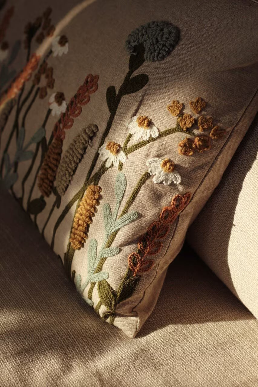 The Strömshaga Cushion Cover Elodie, 40 x 60 cm, features beige fabric embroidered with earthy-toned flowers and adds elegance to a matching beige sofa.
