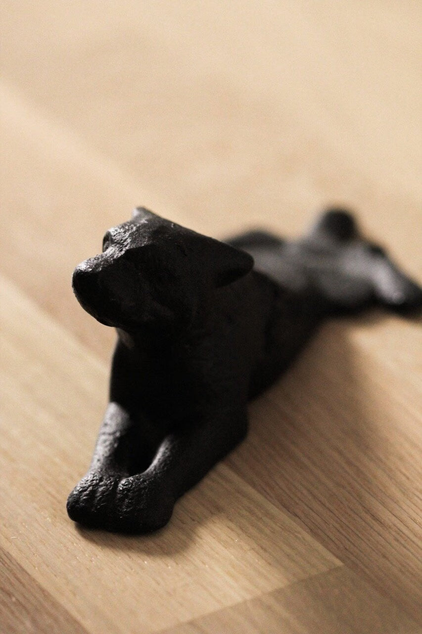The Strömshaga Door Stopper Dog, crafted in cast iron with a matte black finish and soft, rounded features, adds decorative charm and practical function when placed on a light wooden surface.