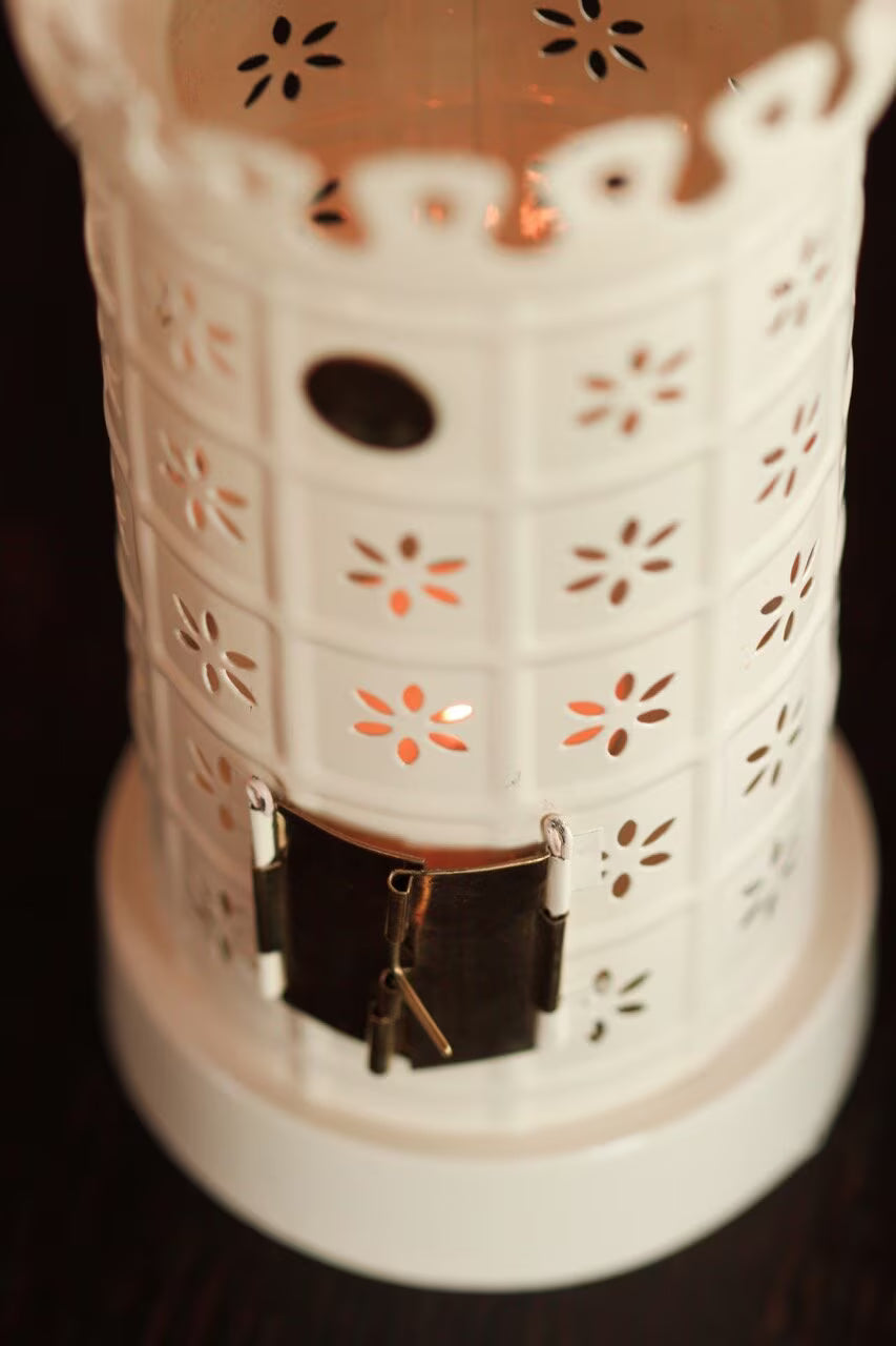 A close-up of Strömshaga’s Tea Light Holder, Tiled Stove in White, featuring floral cutouts, a small door, and keys hanging in front. This decorative lantern glows warmly through its patterns, creating a cozy ambiance.