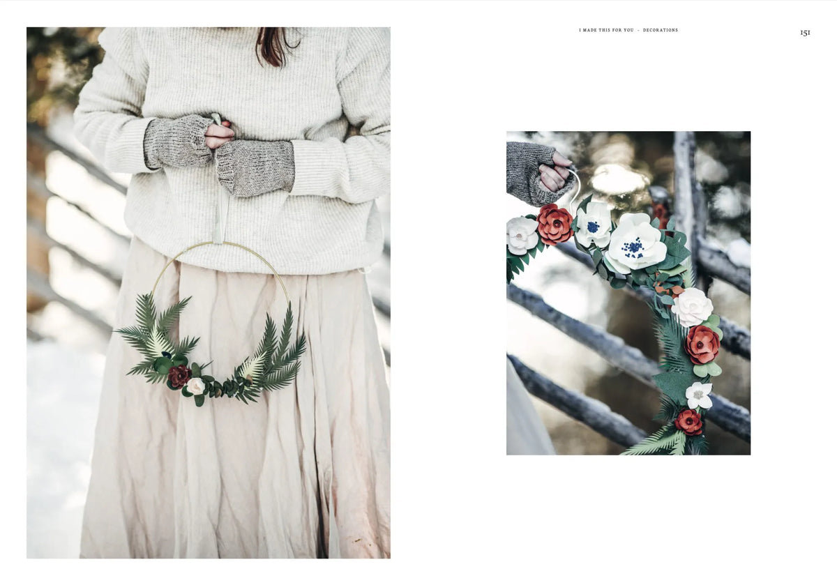 A person dressed in a beige sweater and skirt holds “I Made This for You – Christmas Gift and Decorations Crafted with Love” by Cozy Publishing, featuring a holiday wreath adorned with green leaves and red and white flowers. Beside them, a close-up displays the handmade Christmas wreath against a backdrop of wooden fencing and snow, highlighting the joy of crafting heartfelt decorations.