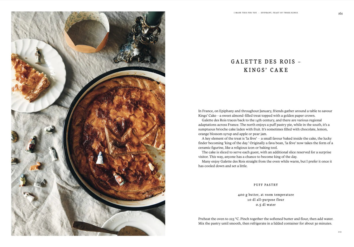A round galette des rois rests on a plate next to a knife and slices of cake on a table adorned with scattered figurines, capturing the warmth of homemade Christmas gatherings. On the right page, “I Made This for You – Christmas Gift and Decorations Crafted with Love” by Cozy Publishing provides the recipe alongside a brief history of the king’s cake in English—ideal for anyone who delights in crafting decorations or seeking heartfelt holiday gifts.