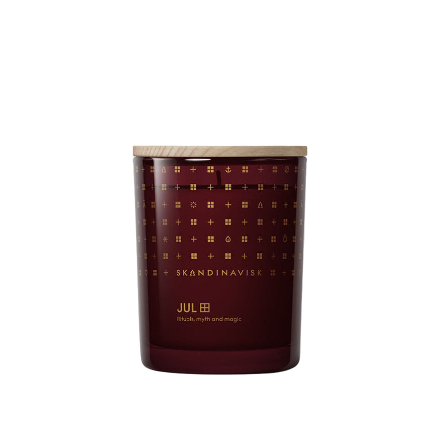 A Skandinavisk Seasonal Jul Scented Candle (50h, 200g)—red with gold motifs and a wooden lid—sits on a white background, its gingerbread scent and “Rituals, myth and magic” label evoking Scandinavian Christmas warmth.