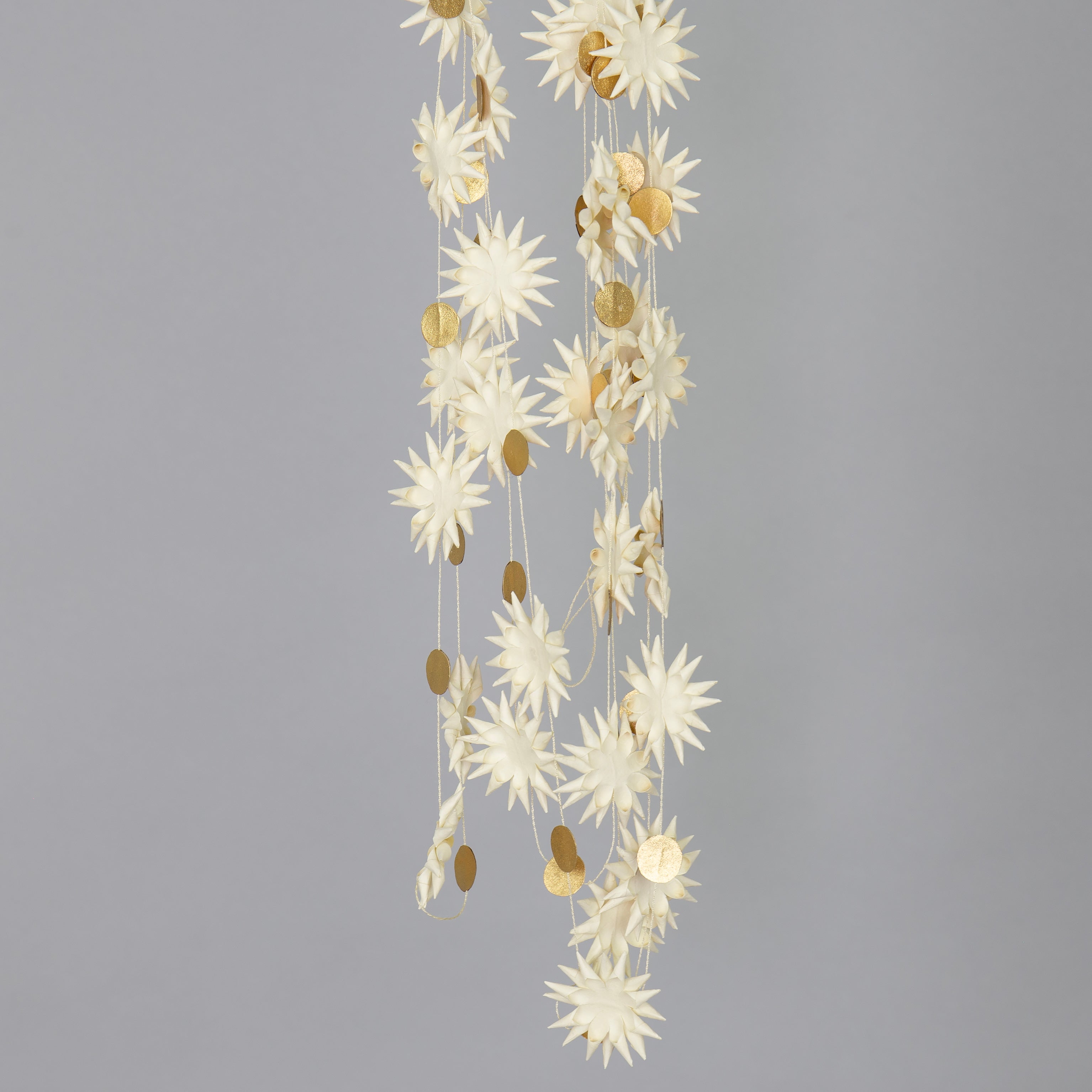 The Kotte Garland in White & Gold by A World of Craft features handmade paper with spiky white, flower-like shapes and small gold circles strung together, creating an eco-friendly decoration.