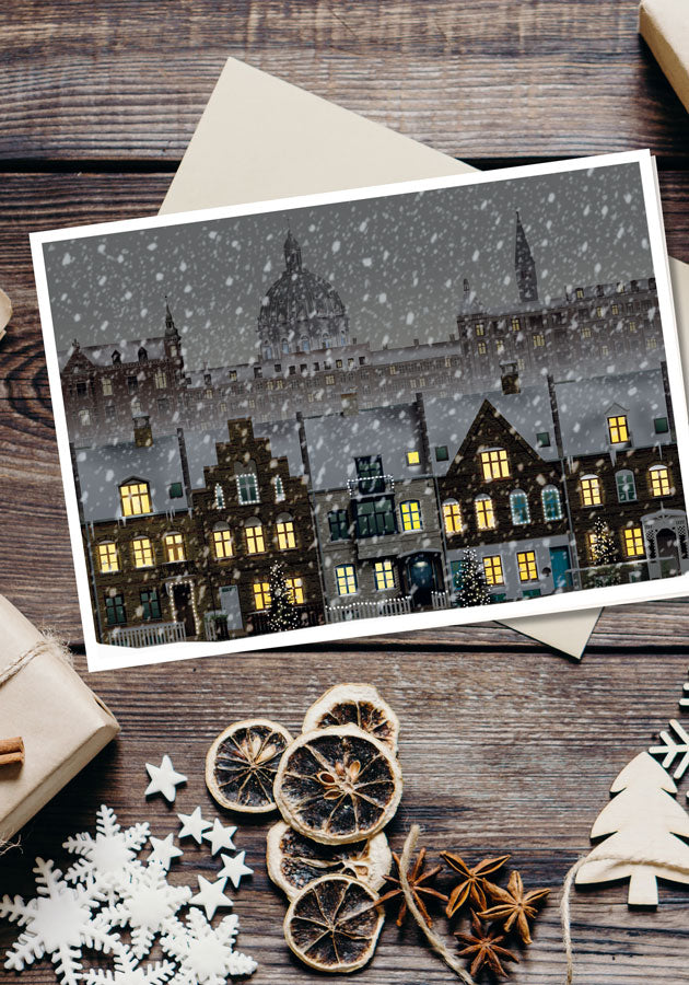A Martin Schwartz “Christmas in Copenhagen, Kartoffelrækkerne” card rests on an envelope, surrounded by dried orange slices, white snowflake ornaments, twine, and a wrapped gift—all artfully arranged on a wooden table.