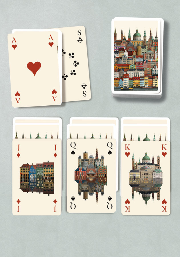 Playing Cards Copenhagen by Martin Schwartz showcases vibrant illustrations of European-style buildings. Some cards are face up, displaying hearts, clubs, queens, and kings adorned with stunning cityscape artwork, while others are stacked face down in tidy piles. This beautifully crafted deck is an ideal gift for anyone who appreciates unique design and fine craftsmanship.