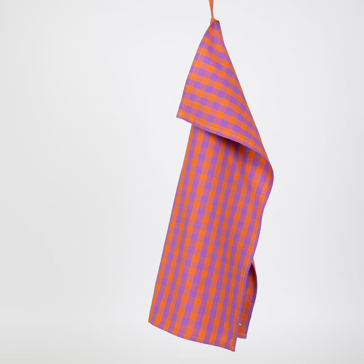 A World of Craft’s handwoven Tea Towel, Nina Purple & Orange in organic cotton, hangs from an orange loop against a plain white background.