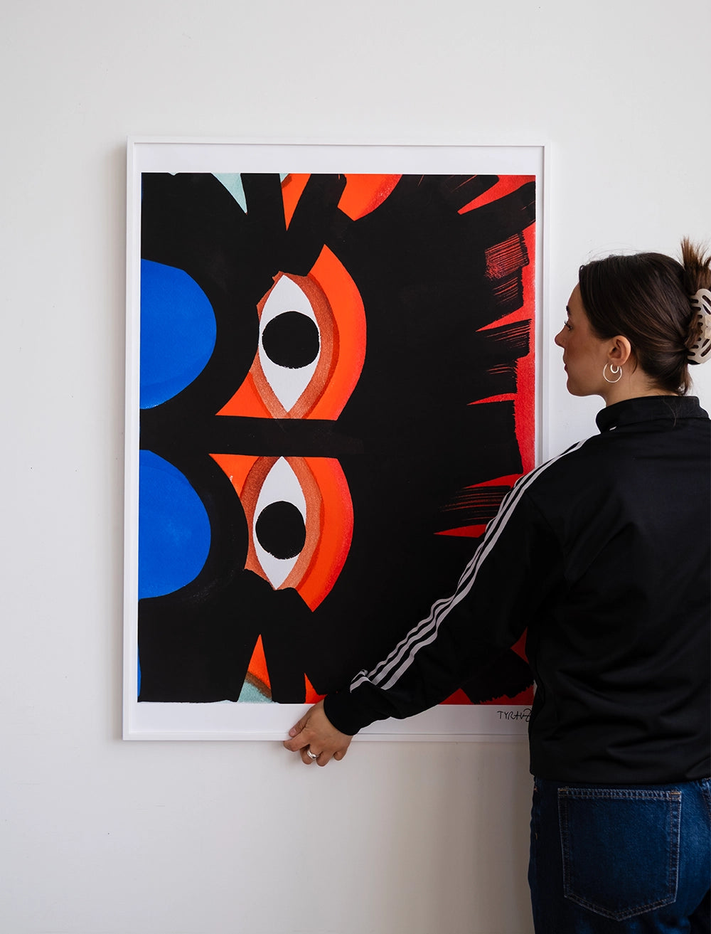 A person in a black jacket holds the Eyes Print by Tyra von Zweigbergk, 50 x 70 cm from Fine Little Day—a bold, colorful abstract artwork with red, blue, orange, and black shapes inspired by playful gouache styles.