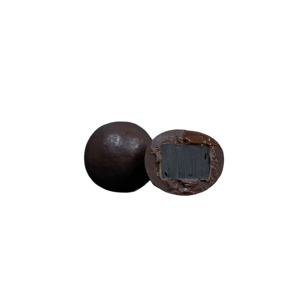 Two round candies from Lakrids by Bülow’s Dark & Sea Salt Liquorice (Small, F) are displayed against a plain white background; one is whole while the other is halved to reveal a black liquorice center encased in dark chocolate. A touch of sea salt enhances their rich, layered flavors.