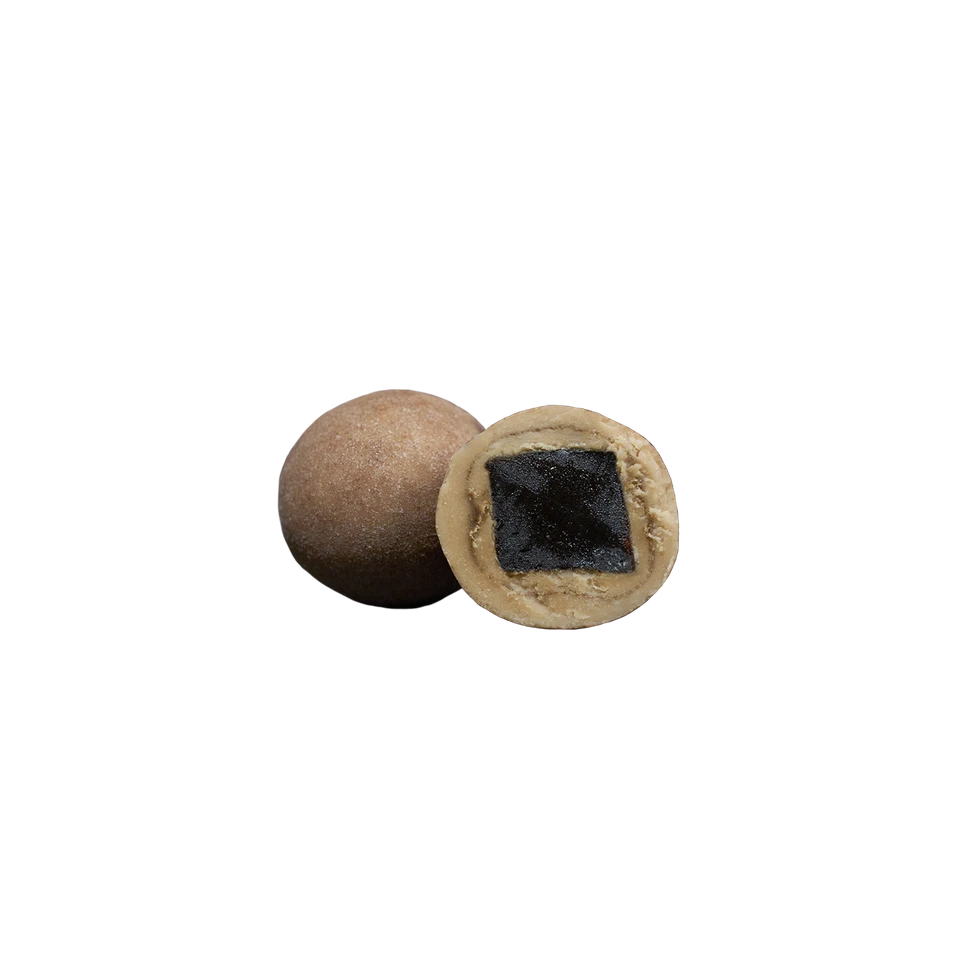 Two round, brown Salt & Caramel Liqourice candies from Lakrids by Bülow are displayed against a plain white background. One piece is whole, while the other is sliced in half to reveal its dark, square-shaped salted caramel liquorice filling.