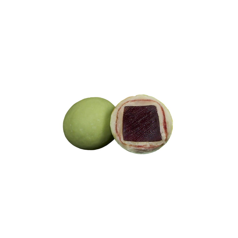 Two round confections from Lakrids by Bülow: one whole Sour Strawberry Liqourice (Small, C) with a green exterior reminiscent of green strawberries, the other cut open to reveal layers of green and white with a square-shaped dark filling inside.