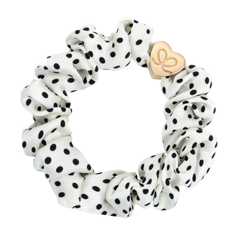 The ByEloise Silk Scrunchie in Polka Dot Black & White features a chic design and is accented with a delicate gold heart charm for added elegance.