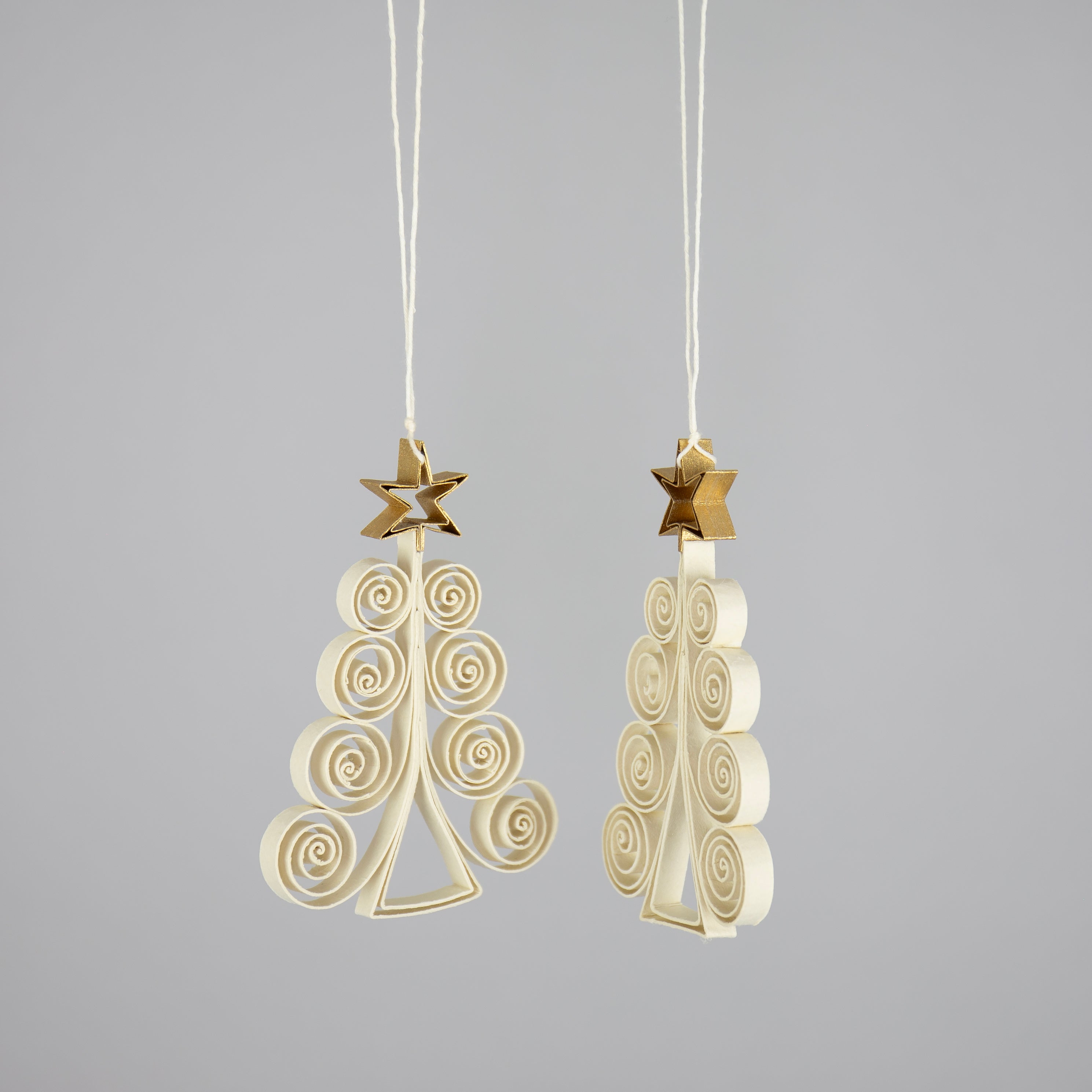 A World of Craft Quilled Fir Tree Christmas Ornaments, 2 Pack in Beige and Gold, feature spiral-shaped, handcrafted designs topped with gold stars and hang from strings against a plain gray background.