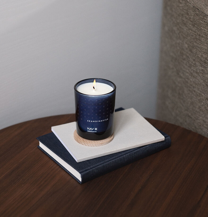 The Skandinavisk Scented Candle Hav 50h, 200g, in a dark glass container, rests on two stacked hardcover books atop a wooden surface.