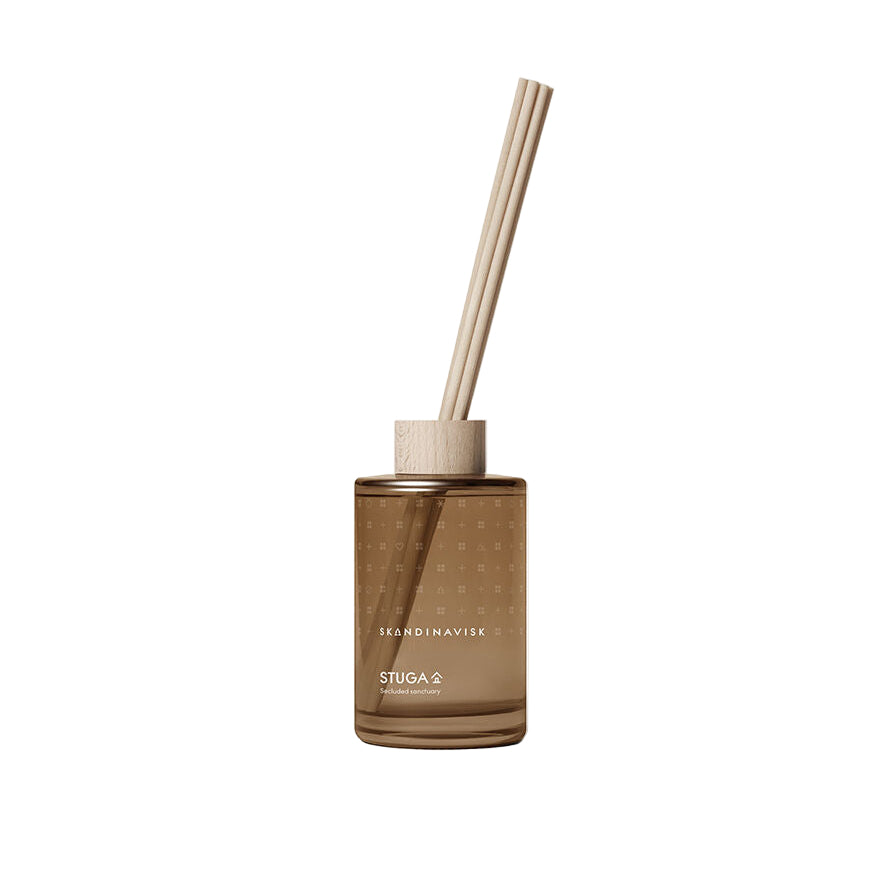 The Skandinavisk Scent Diffuser Seasonal Stuga, 200ml, features a brown glass bottle with wooden cap and three reed sticks, filling your space with vegan fragrance.