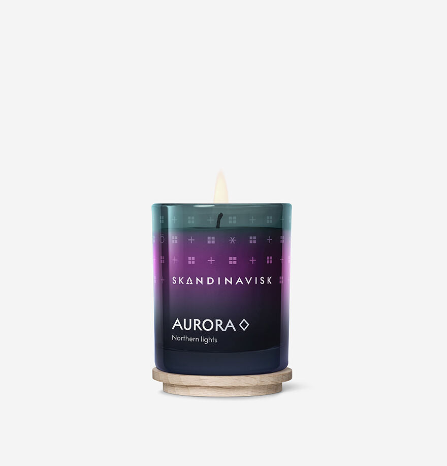 The Seasonal Aurora Scented Candle 20h, 65g by Skandinavisk glows in a gradient glass holder with Swedish rapeseed wax, releasing sandalwood and juniper berry notes against a plain white background.