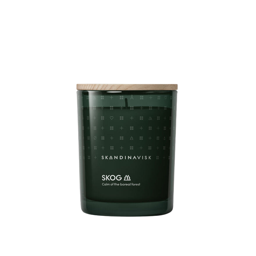 The Skandinavisk Scented Candle Skog 50h, 200g features a pine needle scent and comes in dark green glass with a wooden lid. Its label reads "Calm of the boreal forest" and it is crafted from Swedish rapeseed wax.