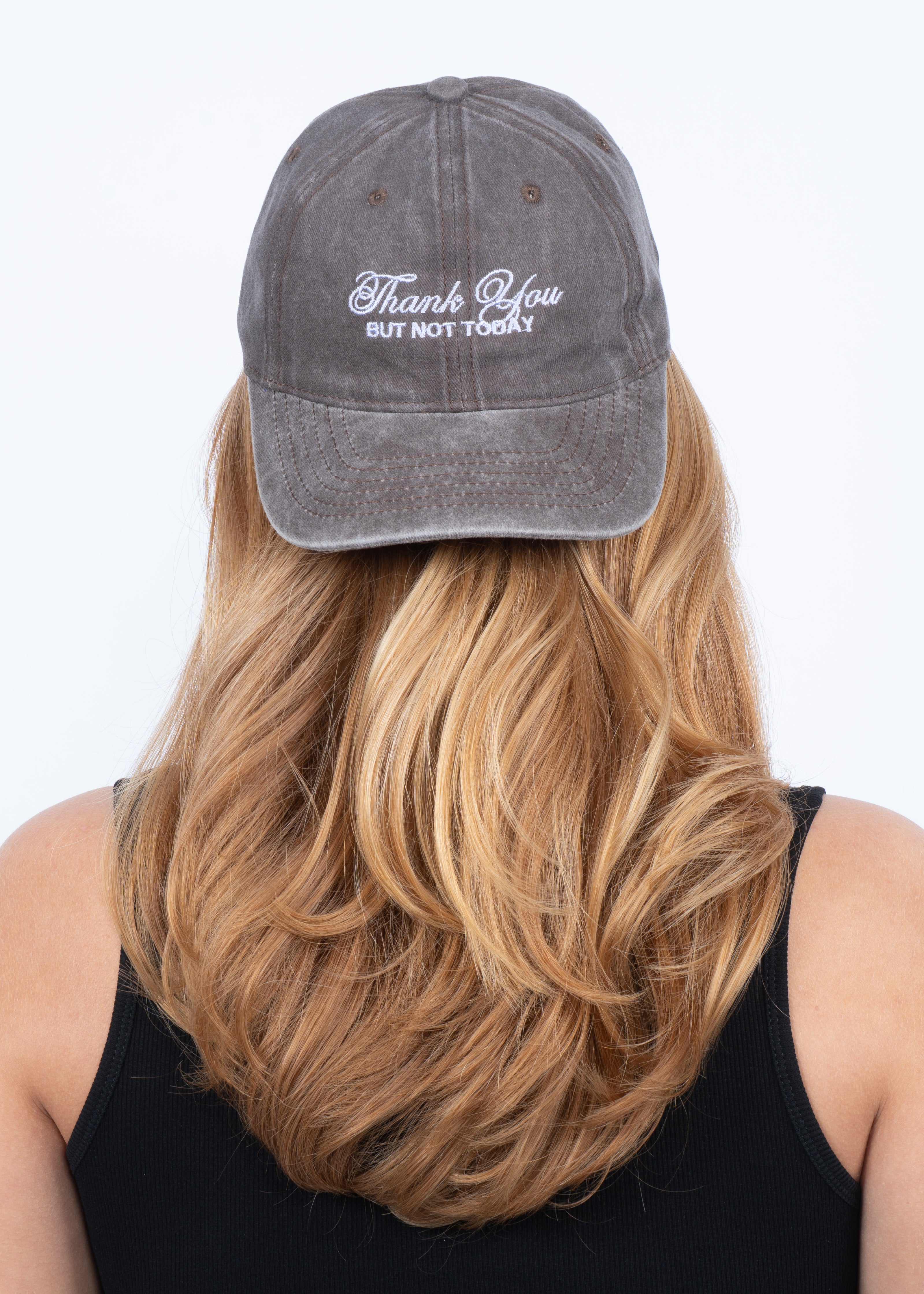 A person with long blonde hair, seen from the back in a black tank top, models the Sui Ava Soft Served Cap in Faded Chocolate Brown with "Thank You but Not Today" embroidered in white, shown against a plain white background.