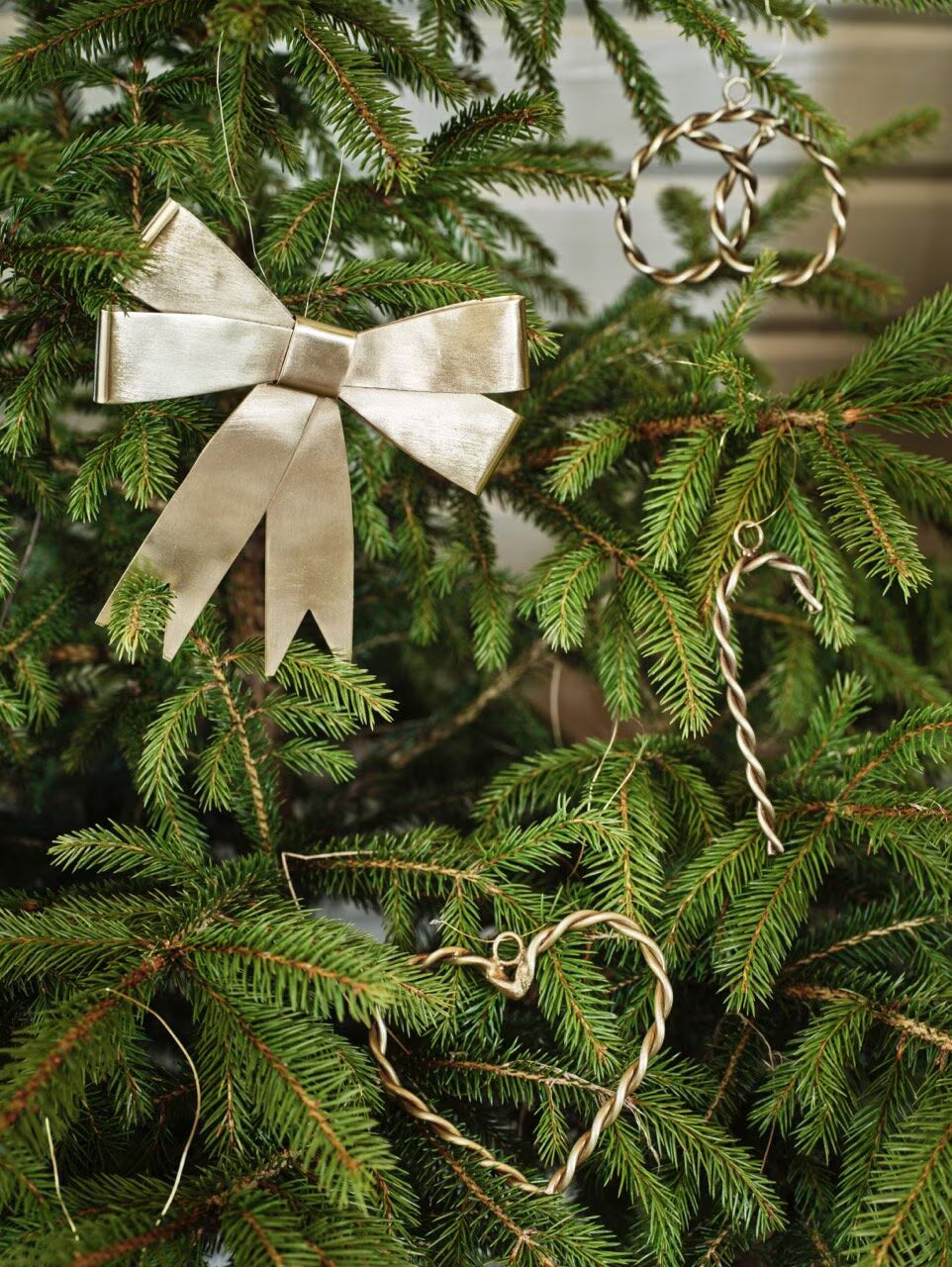 A Christmas tree adorned with Strömshaga’s Ribbon Hanging Ornament in gleaming brass, alongside decorative ribbons and ornaments crafted from twisted gold wire in the shapes of a wreath, candy cane, and heart, creates an extra festive display.