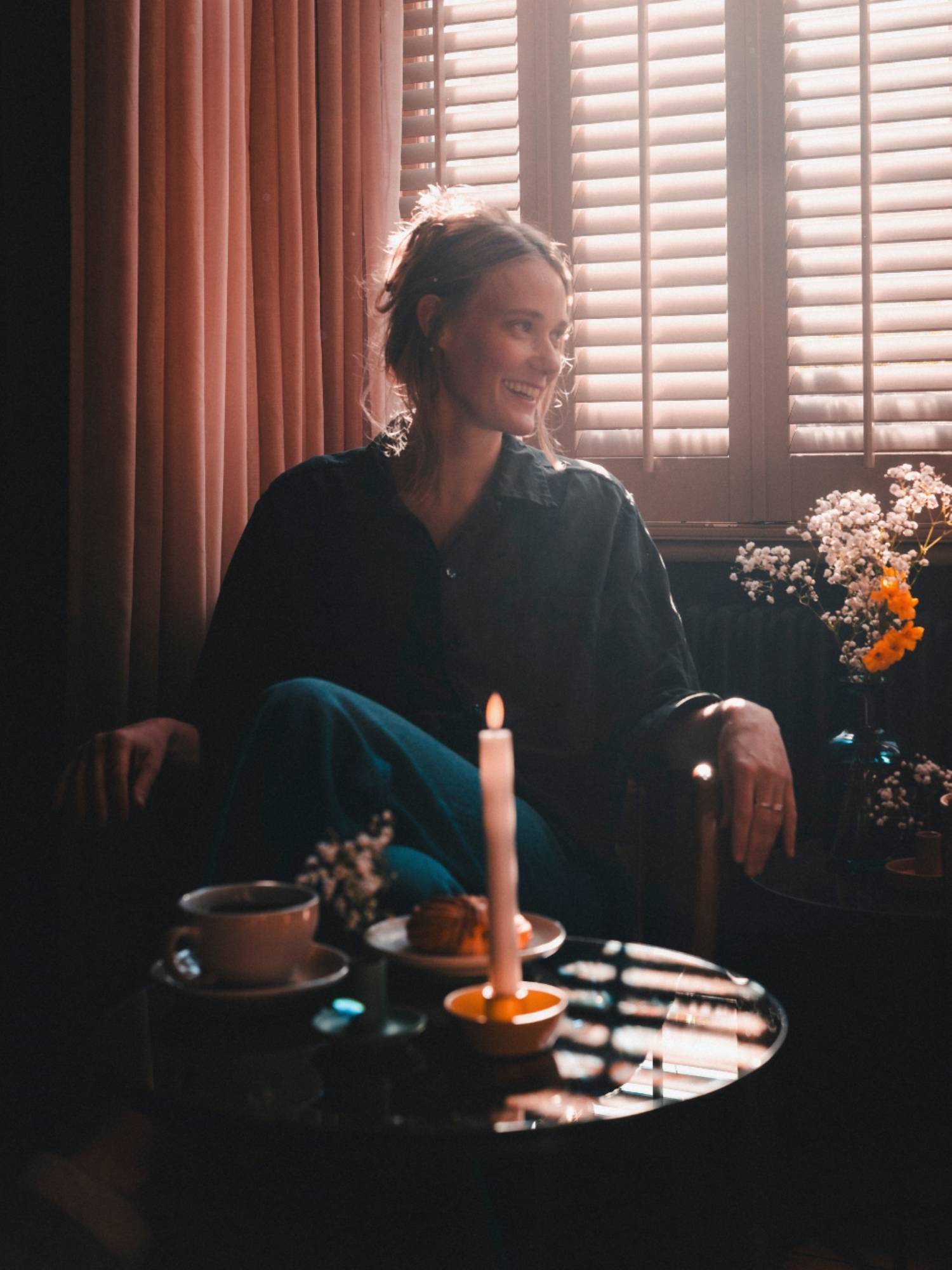 Woman sitting at a table with a candle and food, in a dimly lit room.