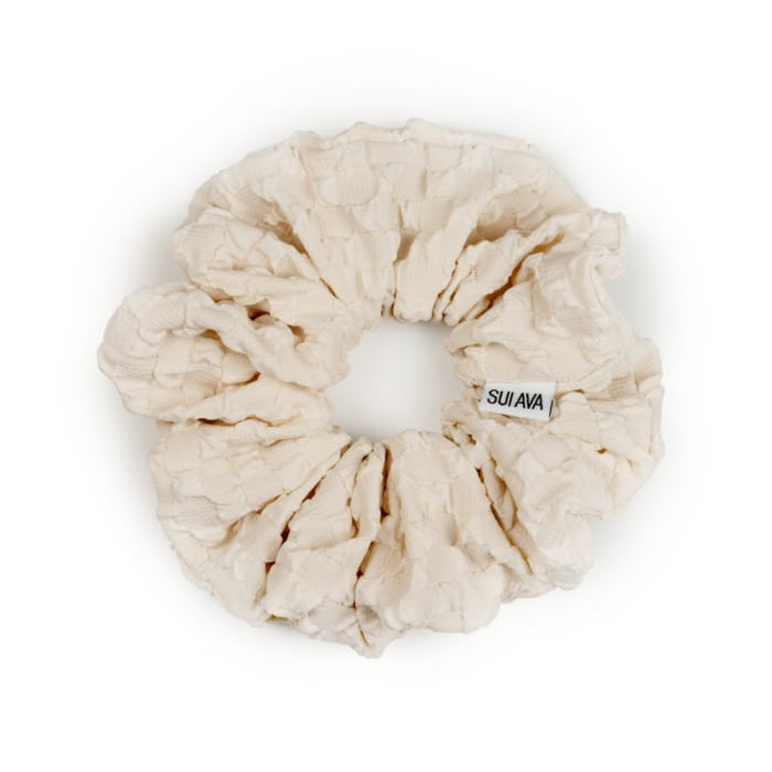 Cream-colored Daydream Scrunchie in Oat Milk made of textured fabric, featuring a small Sui Ava label attached to the elastic band.