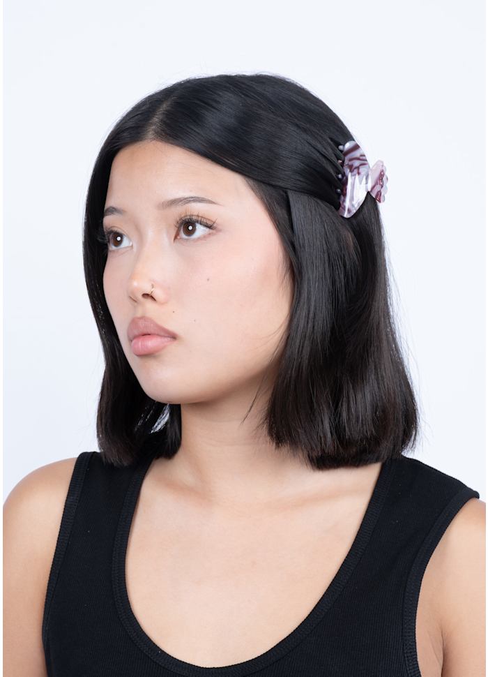 A person with dark hair wears a small, pink and purple marbled Lene Ember Mini Hair Claw Clip by Sui Ava on the side of their head for a secure hold.