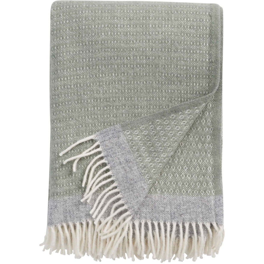 Introducing the Harald Eco Lambswool Throw in Green & Grey by Klippan Yllefabrik—a folded sage green and grey woven blanket featuring a subtle dotted pattern and white fringe along the edge. Crafted from organic lamb’s wool, this classic throw makes a cozy addition to your home décor.