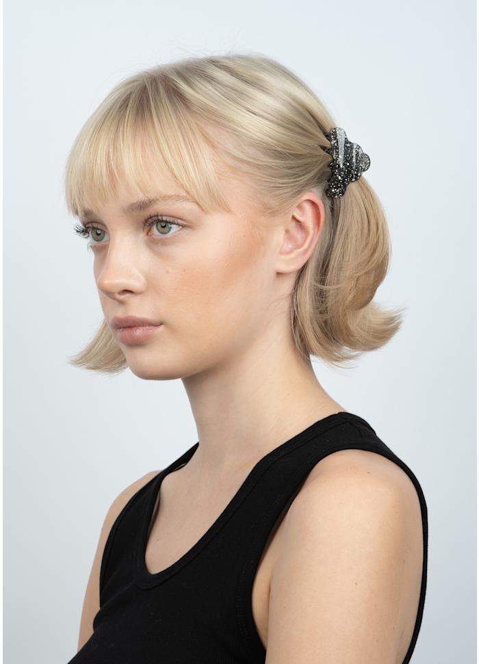 A person with blonde hair wearing a small, black Sui Ava Lene Glitter Mini Hair Claw Clip in Black Diamond.