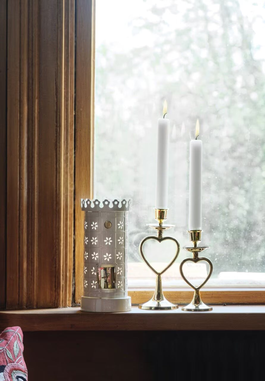 A Strömshaga Tea Light Holder, Tiled Stove in White, and a white lantern sit on a wooden windowsill before a foggy window with greenery outside.