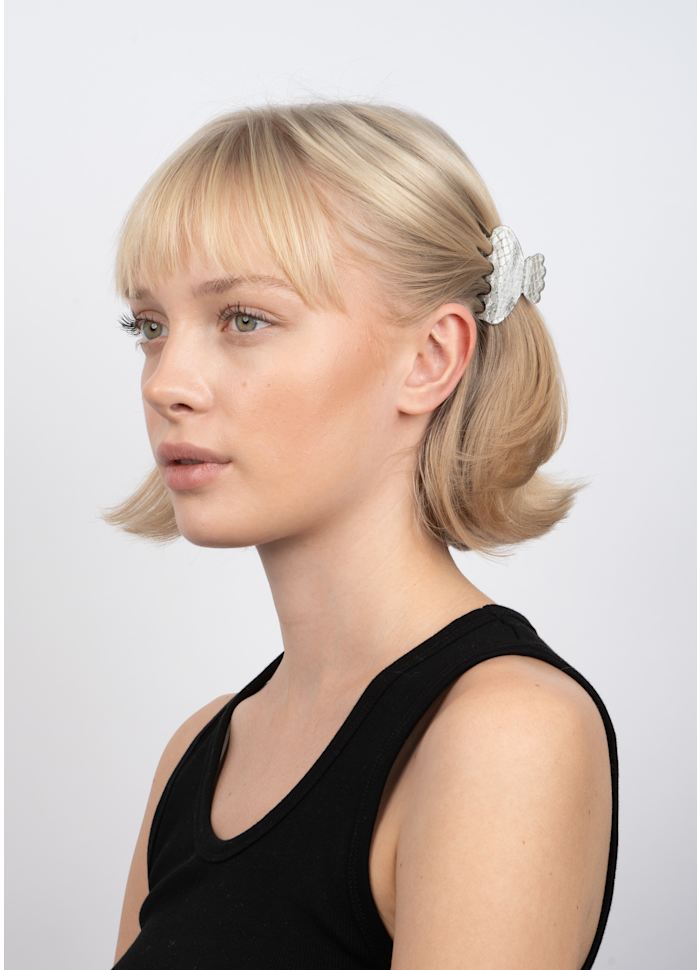 A silver Helle Snake Mini Hair Claw Clip by Sui Ava with a snakeskin texture worn in the side of a person’s hair.