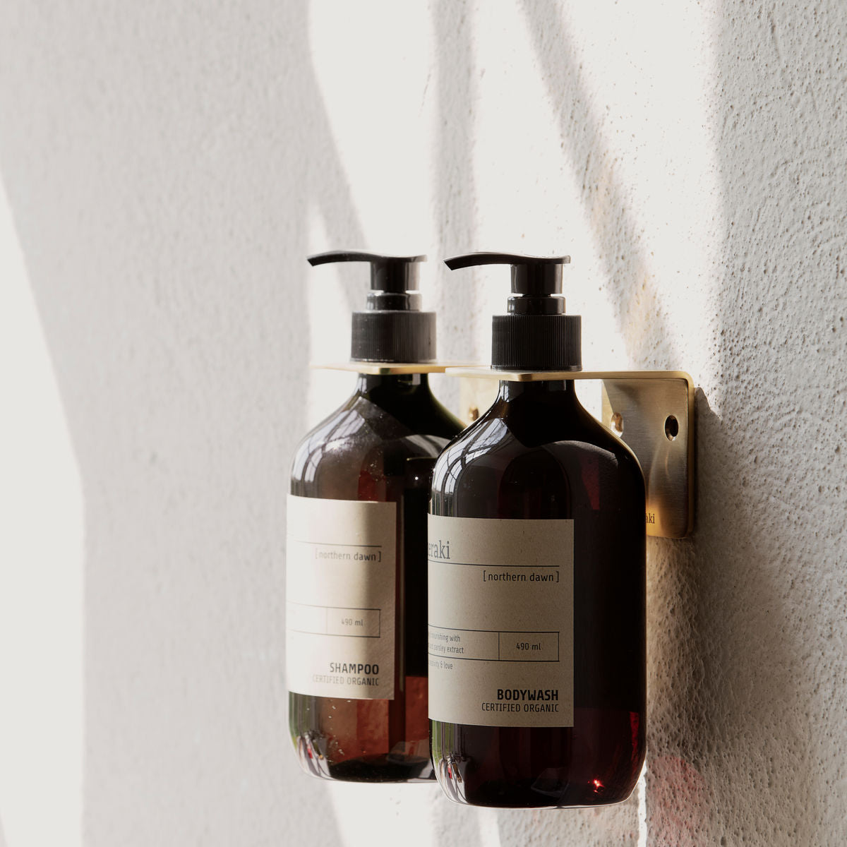 A set of Meraki Body Wash Organic, Northern Dawn bottles with white labels on a white wall, each containing nourishing organic formula for your skin.