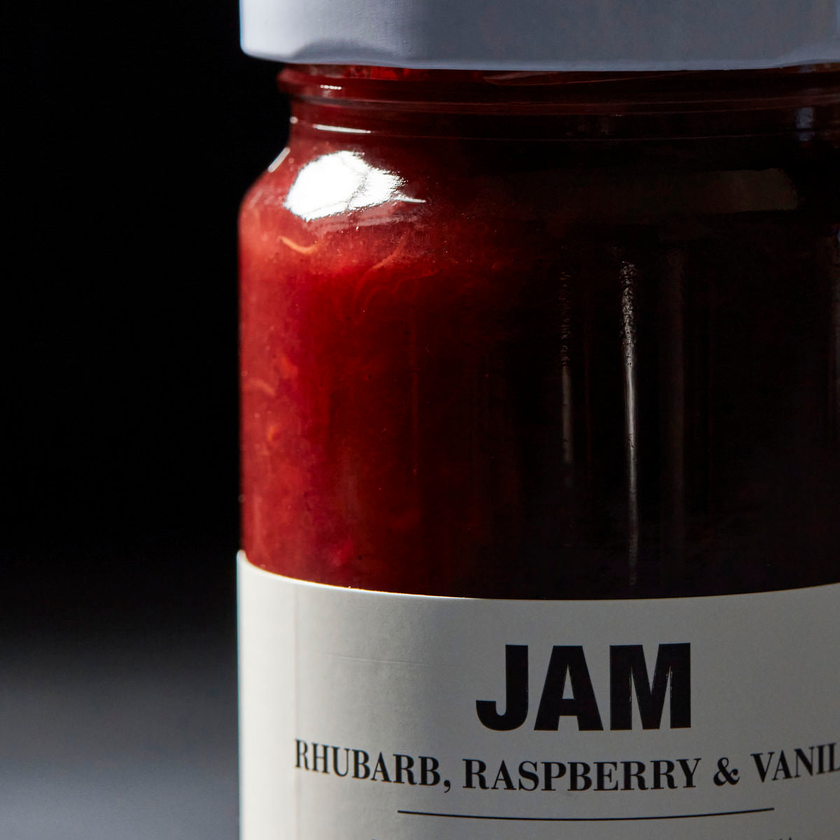A close-up of a glass jar labeled Jam, Rhubarb, Raspberry & Vanilla by Nicolas Vahé, featuring a white lid and filled with red jam.