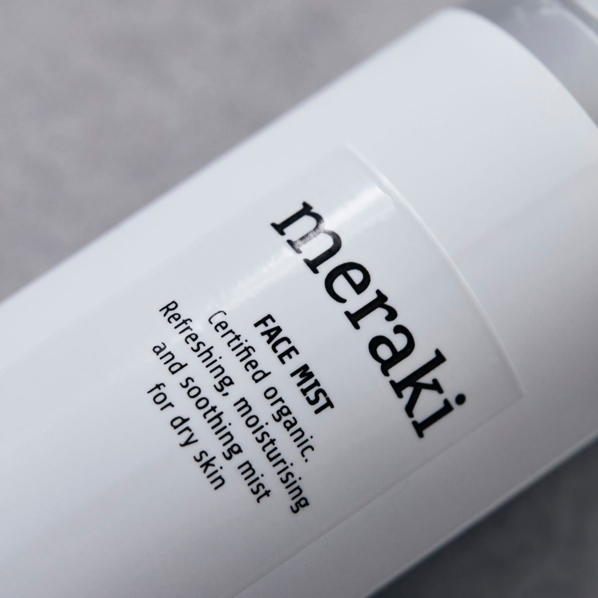 Close-up of a Meraki Face Mist, Organic with Earth Marine Water bottle, featuring a white design with black text. The label highlights it as a certified organic mist that refreshes, moisturizes, and soothes dry skin. Infused with Earth Marine Water to help promote a radiant complexion.