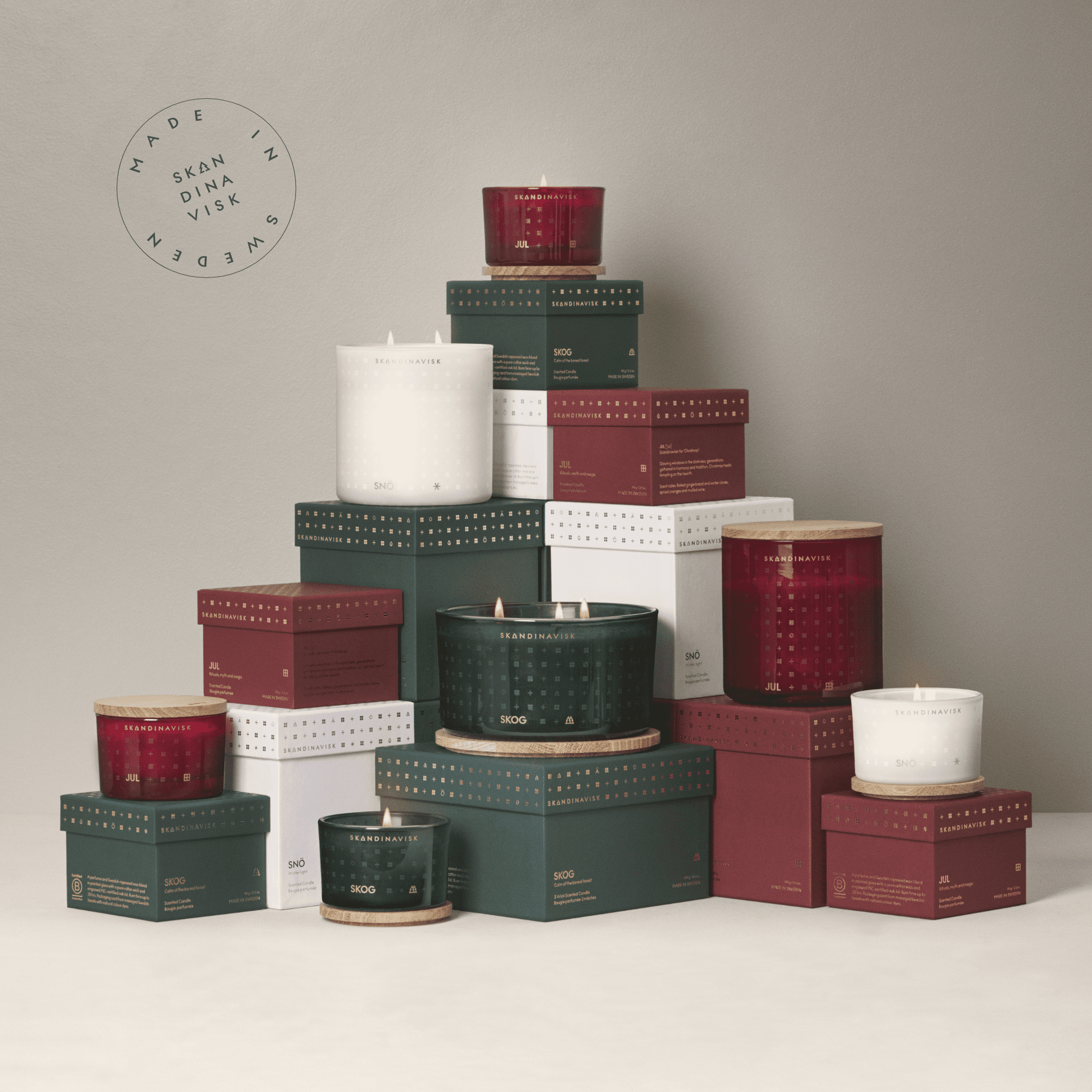 The Skandinavisk Seasonal Jul Scented Candle (2 Wick, 400g) is shown in red jars with matching boxes, pyramid-styled against a neutral background. A circular "MADE IN SWEDEN SKANDINAVISK" stamp appears on the display.
