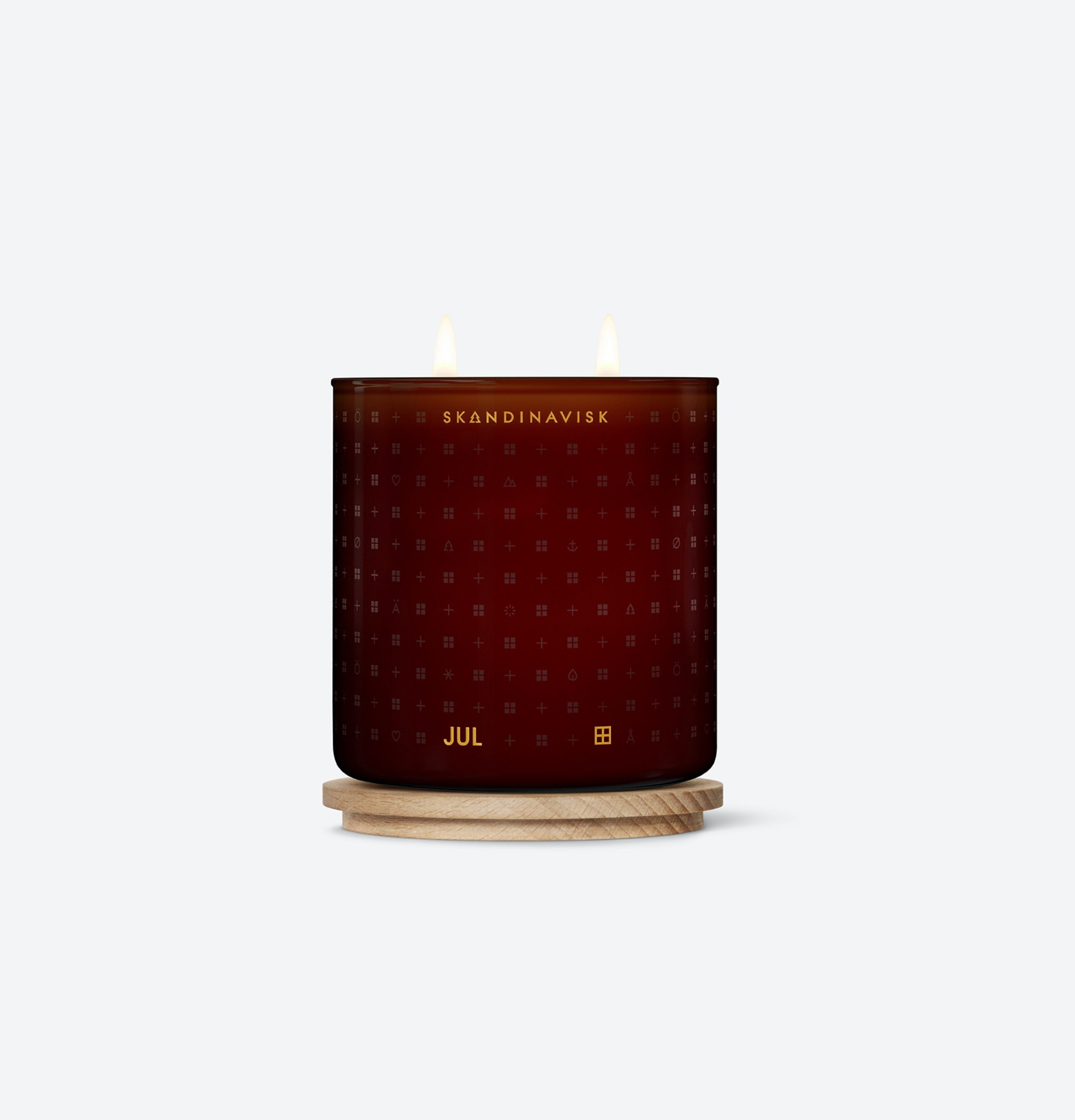 A lit dark red Seasonal Jul Scented Candle, 2 Wick, 400 g by Skandinavisk sits in a labeled glass holder on a light wooden coaster, made from Swedish rapeseed wax, set against a plain white background.