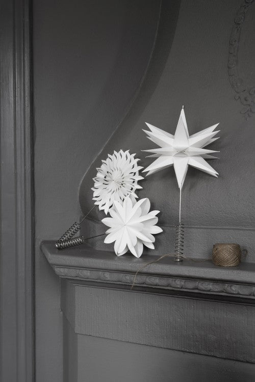 Three Watt & Veke Topstar Sputnik ornaments, each handmade from white paper (25cm), are displayed on a gray mantel with metal springs and twine. One is styled as a modern Christmas tree topper.