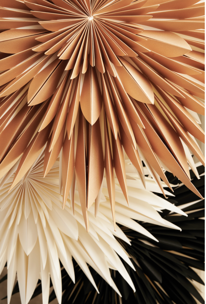 Close-up of layered paper stars, featuring Watt & Vekes Star Maja in Paper, Gold 60cm in a box, displayed in shades of tan, white, and black.