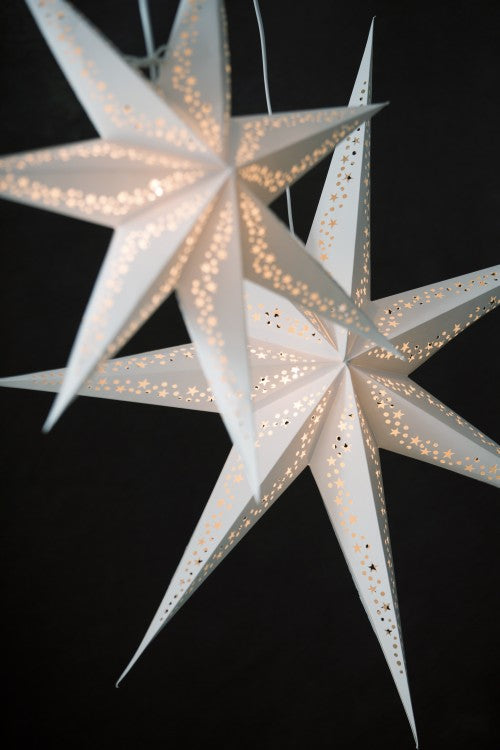 Two Star Vintergatan Christmas White 44cm lanterns by Watt & Veke, each a handmade white paper star with intricate cutouts, glow warmly against a dark background, capturing the cozy charm of Nordic nights.